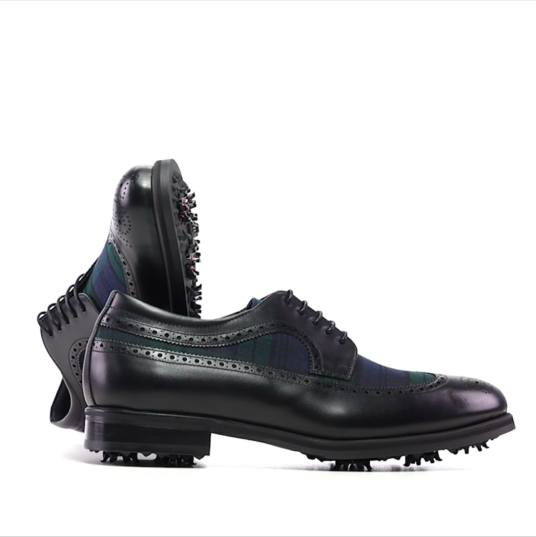 A pair of handmade black leather golf shoes with Black Watch tartan on the vamps, side on view showing the lace-up closure and round toes.