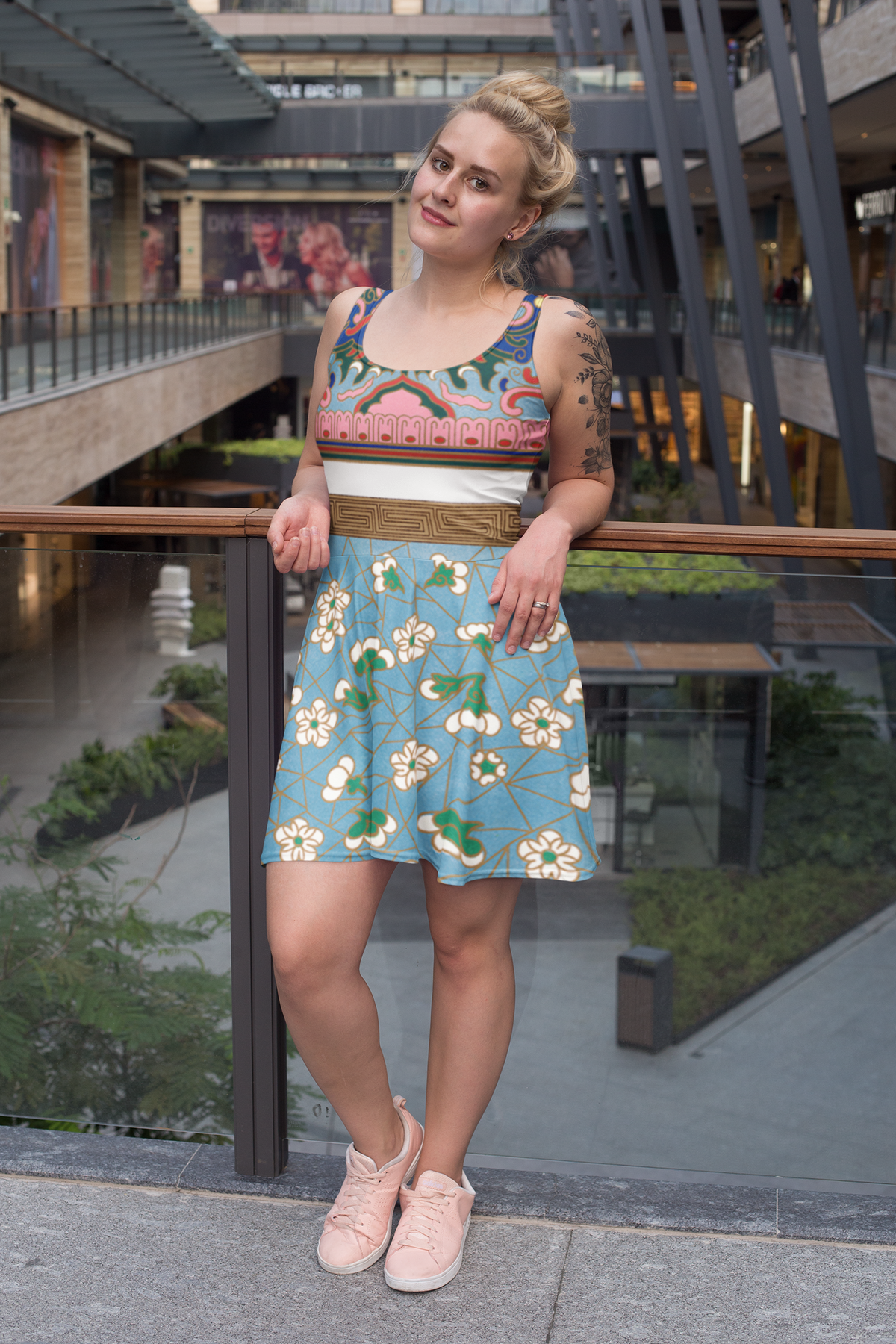 A woman wearing a vintage Art Nouveau-inspired skater dress with a floral and geometric pattern, in a blue and green color palette, standing on a terrace.